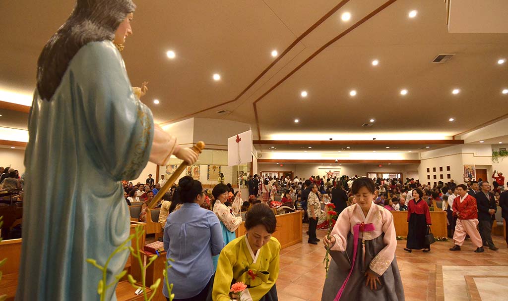 Korean women place flowers at a statue of Mary.