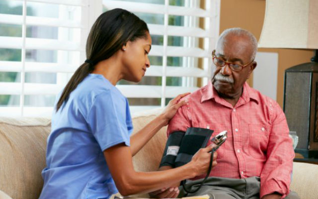 A home health care worker checks a man's blood pressure