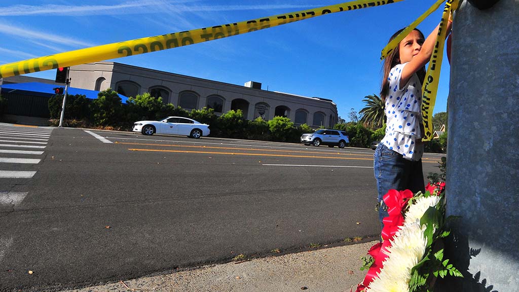 A young girl attaches hearts to a light pole across the street from Chabad of Poway.