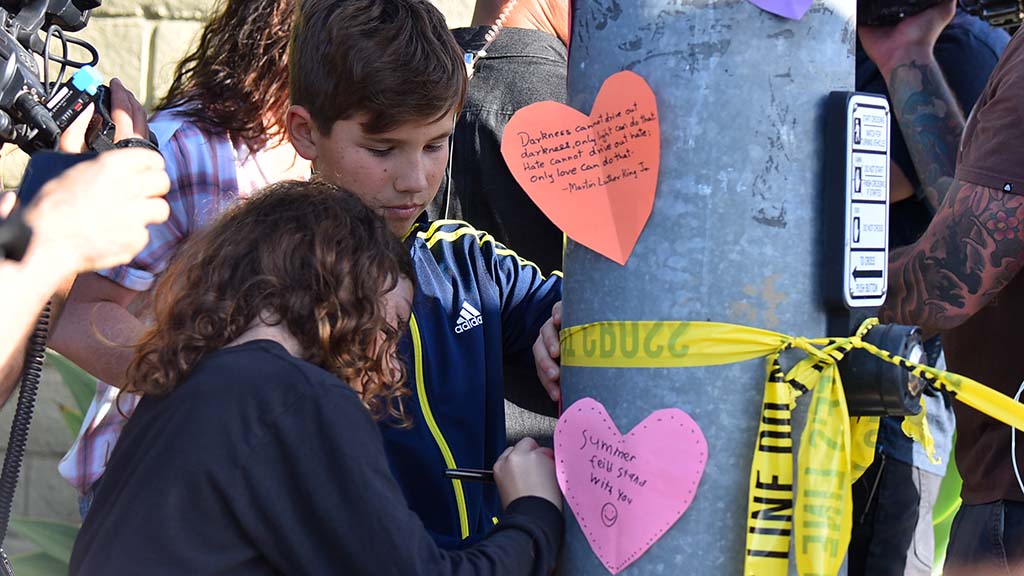 Two children put up hearts on a light pole across the street from Chabad of Poway.