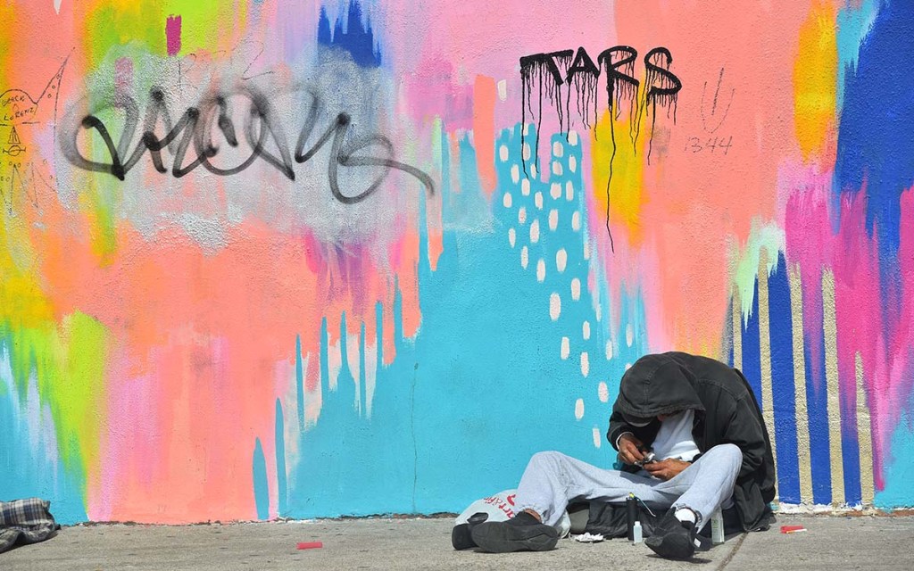 A homeless man sits against a brightly covered wall across the street from San Diego City College. Photo by Chris Stone